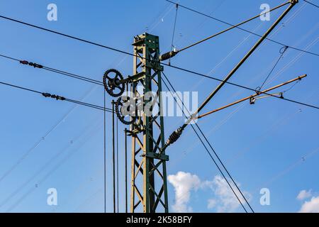 Cavi, staffe e ingranaggi su un palo metallico per linee aeree per treni elettrici contro un cielo blu Foto Stock