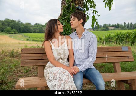 Due amanti si guardano teneramente negli occhi mentre si siedono sulla panchina durante una passeggiata in campagna. Foto Stock