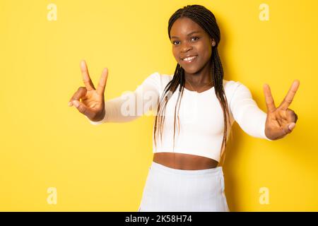 Foto di adorabile giovane donna afro-americana lucida indossare abbigliamento casual mostrando segno V sorridendo isolato sfondo di colore giallo Foto Stock