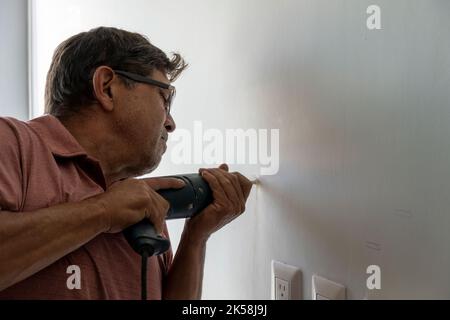 latino uomo utilizzando un trapano elettrico per praticare fori nella parete per appendere un nuovo televisore, trapanando fori nella parete, messicano, ispanico Foto Stock