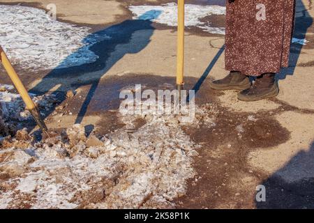 Una donna operatrice pulisce il ghiaccio e rimuove la neve dalle lastre di pavimentazione utilizzando un rompighiaccio. Un uomo rompe il ghiaccio con un frantoio a lame d'acciaio, anche un rompighiaccio Foto Stock