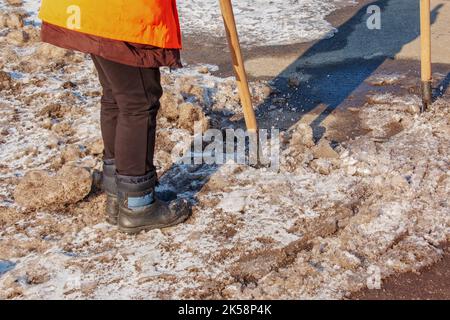 Una donna operatrice pulisce il ghiaccio e rimuove la neve dalle lastre di pavimentazione utilizzando un rompighiaccio. Un uomo rompe il ghiaccio con un frantoio a lame d'acciaio, anche un rompighiaccio Foto Stock