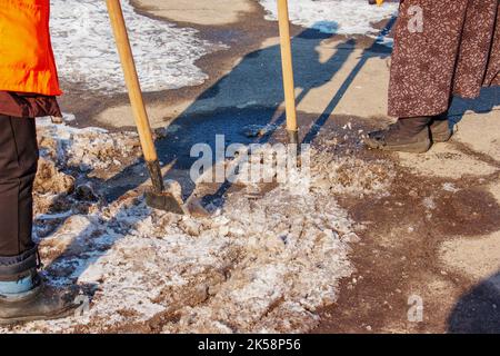 Una donna operatrice pulisce il ghiaccio e rimuove la neve dalle lastre di pavimentazione utilizzando un rompighiaccio. Un uomo rompe il ghiaccio con un frantoio a lame d'acciaio, anche un rompighiaccio Foto Stock