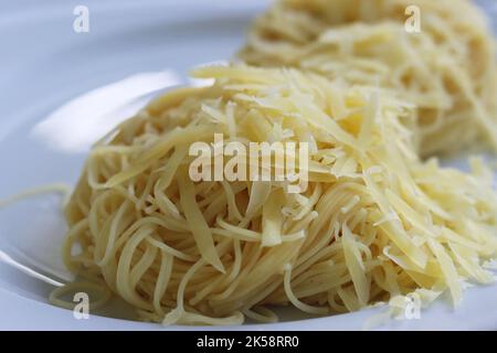 Spaghetti arrotolati con parmigiano grattugiato sul piatto bianco. Vista laterale. Spaghetti cotti in lastra di vetro grigio isolato su fondo bianco Foto Stock