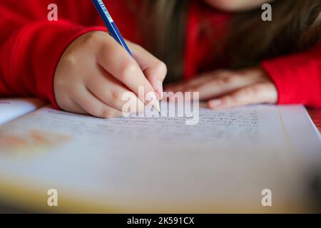 La matita in una mano dei bambini scrive le parole in un taccuino.Homework.schoolgirl fa il suo lavoro. Studio e education.child scrive con una matita in un taccuino Foto Stock