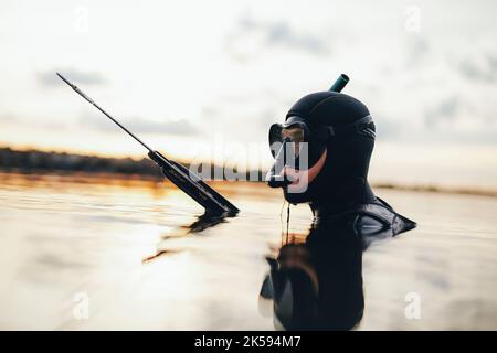 Subacqueo che tiene un fucile mentre è immerso in acqua di mare. Subacqueo maschile a caccia di pesci indossando un'attrezzatura subacquea e una muta. Foto Stock