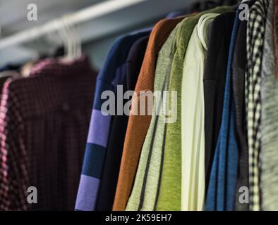 Foto in primo piano delle camicie da uomo appese. Molte camicie appese su una rastrelliera. Abiti maschili, giacche e camicie appesi sul corrimano. Nessuno, sfocato, selec Foto Stock