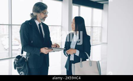 Elegante donna asiatica sta firmando il contratto di affari e parlando con l'uomo caucasico maturo del socio all'interno nell'edificio commerciale. Concetto di bene immobile e di affari. Foto Stock