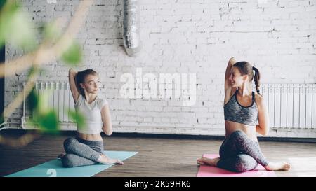 La giovane ragazza bionda sta godendo la pratica individuale di yoga con un'istruttrice femminile amichevole in studio luce. Le donne stanno facendo la sequenza di asana sui tappetini luminosi. Atmosfera accogliente e rilassante. Foto Stock