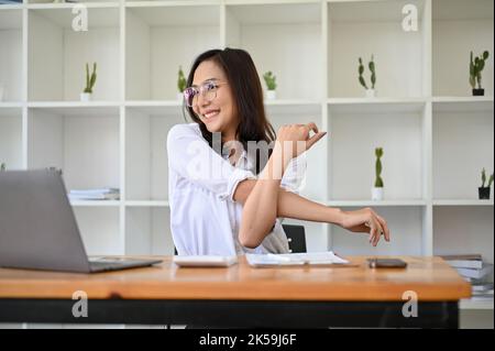 Una donna d'affari asiatica o una lavoratrice d'ufficio, calma e rilassata, si stende le braccia dopo aver finito il lavoro alla scrivania. Foto Stock