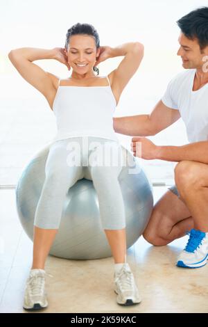 Tornare alle basi del fitness. Un istruttore di fitness che mostra a una giovane donna come fare un esercizio fisico. Foto Stock