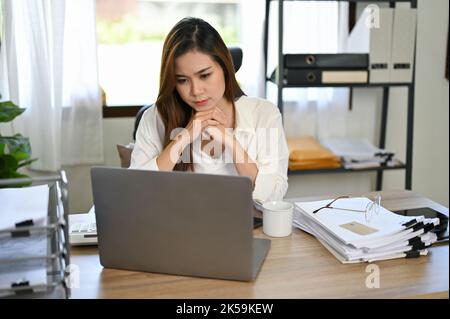 Una donna d'affari o una donna d'affari asiatica premurosa e millenaria che si concentrano sulla pianificazione del suo nuovo progetto, guardando lo schermo del notebook, lavorando alla sua scrivania in t Foto Stock