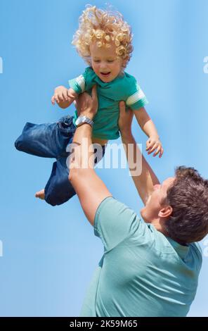 HES in mani sicure. Un padre che dondola il figlio del bambino nell'aria contro uno sfondo del cielo. Foto Stock