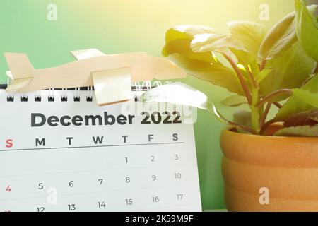 Focus selettivo del calendario da tavolo di dicembre 2022 con modello di aereo e albero di natale su sfondo verde. Vacanze natalizie in viaggio Foto Stock