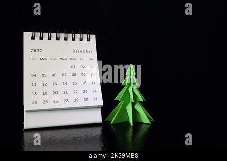 Focalizzazione selettiva del calendario da tavolo di dicembre 2022 su sfondo nero scuro con albero di natale e spazio copia. Foto Stock