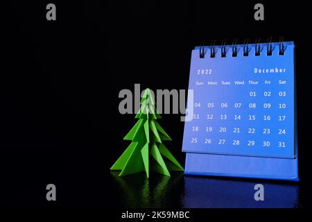 Focalizzazione selettiva del calendario da tavolo di dicembre 2022 su sfondo nero scuro con albero di natale e spazio copia. Foto Stock