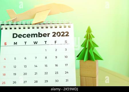 Focus selettivo del calendario da tavolo di dicembre 2022 con modello di aereo e albero di natale su sfondo verde. Vacanze natalizie in viaggio Foto Stock