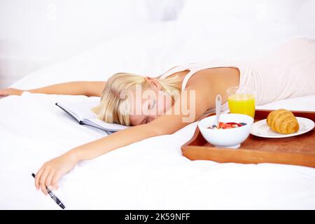 Non posso che dormire oggi. Giovane donna che dorme accanto a un vassoio per la colazione con un diario aperto sdraiato sotto la testa. Foto Stock