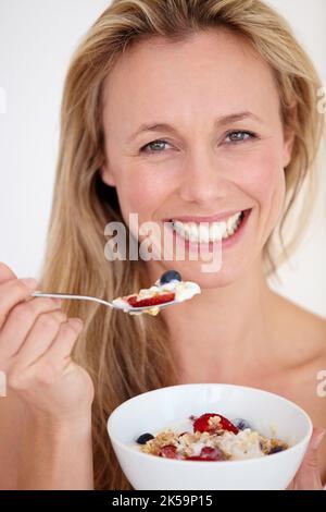 Mangiare sano mantiene la sua giovane. Bella donna sorridente felice mentre si gode una sana ciotola di colazione. Foto Stock