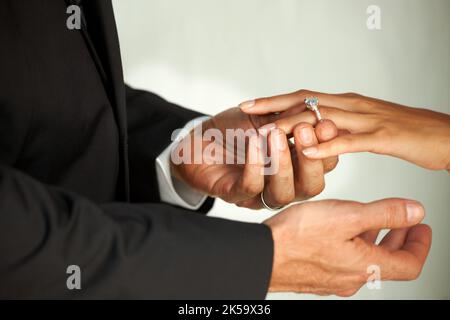 Un impegno che dura tutta la vita. Vista ritagliata di uno sposo che scivola un anello sul dito delle sue spose. Foto Stock