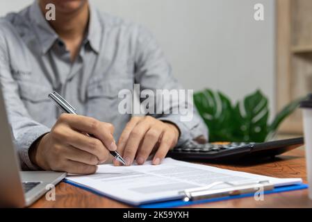 Mano che tiene la penna che scrive la carta di affari documento di investimento finanziario o firma il lavoro di contratto e l'assicurazione sulla scrivania. Foto Stock