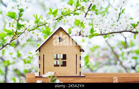 Small wooden house model under a blooming tree branch Foto Stock