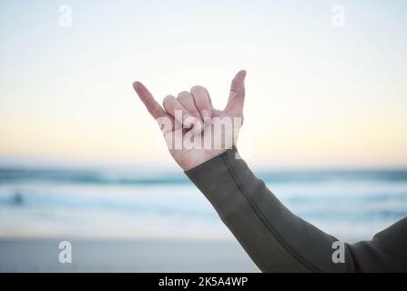 Shaka, surf e sport con il segno mano di un uomo sulla spiaggia per il surf, fitness o esercizio al mattino. Allenamento, allenamento e salute con un Foto Stock