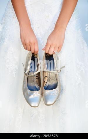 Accessori per matrimoni bellissimi. Una sposa che tiene i tacchi alti davanti a lei. Foto Stock