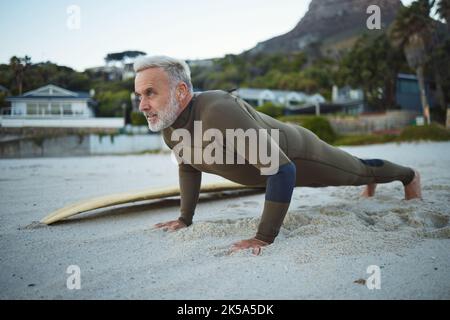 Uomo anziano, spiaggia e fitness in Sudafrica di surfista in esercizio per il riscaldamento di routine mattutino. Anziani maschi in sport di surf e di formazione pushup Foto Stock