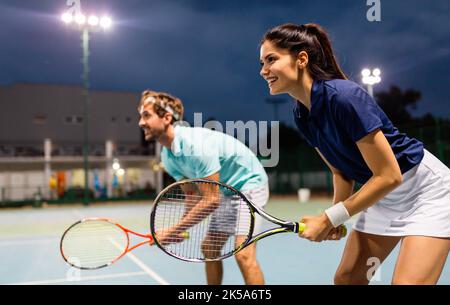 Concetto di persone di sport di tennis. Giocatore doppio misto che colpisce la palla da tennis con il partner in piedi vicino alla rete Foto Stock