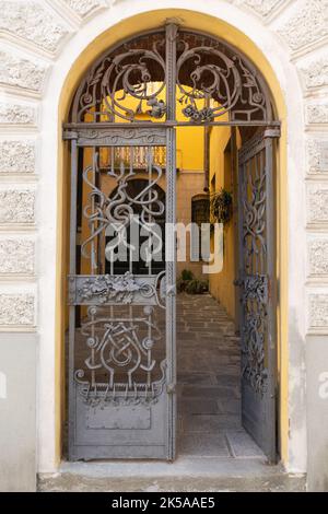 Una porta caratteristica e decorativa in una casa italiana caratterizzata da un cancello di ferro e un arco in pietra. Conduce ad un tipico cortile. Foto Stock