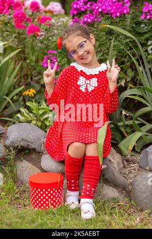 Una bambina divertente in un abito rosso con polka Foto Stock