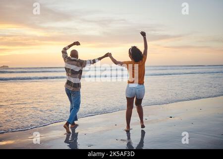 Amore, viaggio e coppia felice in spiaggia godendo vacanze estive o divertente luna di miele al tramonto mentre si tiene le mani ed essere giocoso. Ridere, energia e. Foto Stock