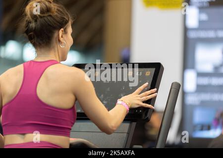 Ragazza che tocca un'esposizione di tapis roulant moderno nel Fitness Club durante il suo allenamento nel Fitness Club. Foto Stock