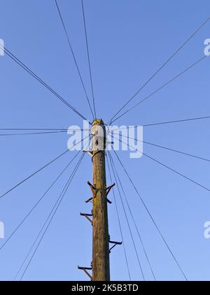 Palo di legno con fili che si irradiano intorno al cerchio intero contro il cielo blu. Foto Stock