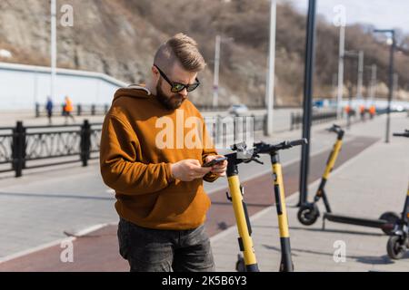 Uomo che utilizza lo smartphone dopo aver utilizzato uno scooter elettrico in città. Trasporto innovativo Foto Stock