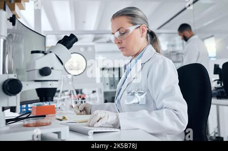 Laboratorio, microscopio e donna che scrivono al computer per dati medici, risultati di test in capsula di Petri o ricerca sul cancro nel settore sanitario. Scienziato maturo, lavoratore Foto Stock