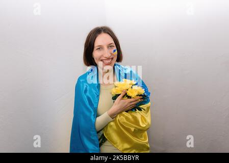 Ragazza giovane con fiori blu e gialli e la bandiera nazionale dell'Ucraina. La bandiera è dipinta sulla guancia della donna. Stop alla guerra. Spazio di copia. Foto Stock