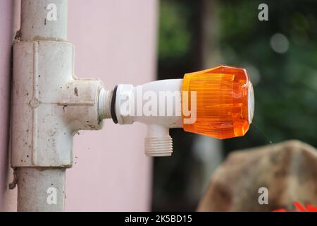 Rubinetto o rubinetto d'acqua in plastica con manopola girevole arancione fissata su un tubo d'acqua in PVC fissato a una parete Foto Stock
