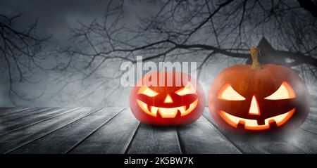 Due pazzi zucche di Halloween, Jack o Lantern, con facce malvagie e occhi su un tavolo di legno con sfondo grigio misty. Zucche di Halloween con dar Foto Stock