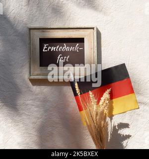 Happy Germany Thanksgiving Day o Erntedankfest in lingua tedesca. Bandiera tedesca e mazzo di spighe di grano su tessuto beige. Piano di giacitura, vista dall'alto. Foto Stock