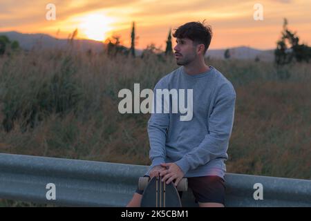 Ritratto di un giovane uomo con uno skateboard al tramonto Foto Stock