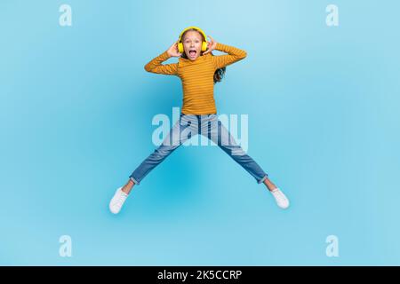 Foto full size di ragazza eccitato vestito giallo jeans pantaloni pullover volo jumping impressionato playlist isolato su sfondo di colore blu Foto Stock