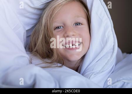 bambina senza denti frontali sorridente la mattina a letto Foto Stock