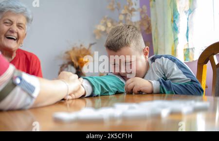 il ragazzo è seduto al tavolo, tenendo la mano della nonna e sorridendo. la bisnonna siede sullo sfondo, sorridendo con orgoglio. famiglia tim Foto Stock