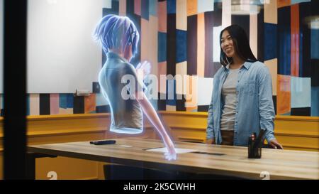 Un avatar di una ragazza dà presentazione ad una donna asiatica attraverso uno schermo astratto ologramma in metaverse. Tecnologia del mondo digitale in parallelo a quello fisico. Realtà aumentata. Foto Stock
