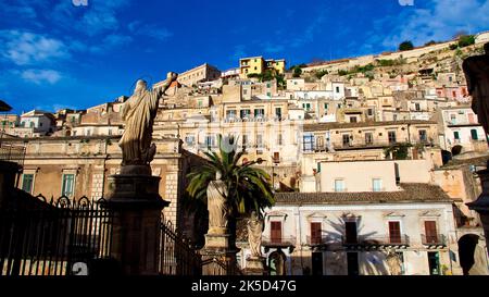 Italia, Sicilia, angolo barocco, città barocca, Modica, città vecchia, luce del mattino, vista dalla cattedrale sul lato opposto della collina costruita, edifici della città vecchia, cielo blu con poche nuvole bianche Foto Stock