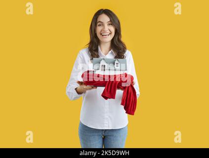 Donna tiene la casa giocattolo avvolto in sciarpa calda come simbolo per il sistema di riscaldamento o freddo inverno nevoso. Foto Stock