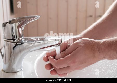 L'uomo lava le mani sotto un flusso di acqua corrente pulita, sopra il lavandino, nel bagno. Concetto di igiene e salute. Foto Stock