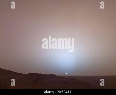 Il 19th maggio 2005, Mars Exploration Rover Spirit della NASA catturò questa vista mozzafiato mentre il Sole affondava sotto il bordo del cratere di Gusev su Marte. Questo mosaico della telecamera panoramica è stato preso intorno alle 6:07:00 nella sera del giorno marziano 489th di rover, o sol. Altre immagini hanno mostrato che il crepuscolo rimane visibile, ma sempre più debole, fino a due ore prima dell'alba o dopo il tramonto. Il lungo crepuscolo marziano (rispetto a quello terrestre) è causato dalla luce solare diffusa intorno al lato notturno del pianeta da abbondante polvere ad alta quota. Una versione ottimizzata delle immagini NASA. Credito NASA/JPL Foto Stock